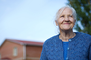 Focused on senior woman with windblown hair, wearing blue sweater, looking off in the distance with a smile