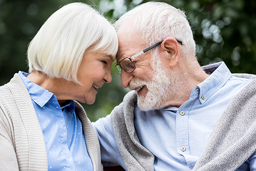Elderly couple sitting outside with foreheads touching and smiling at each other